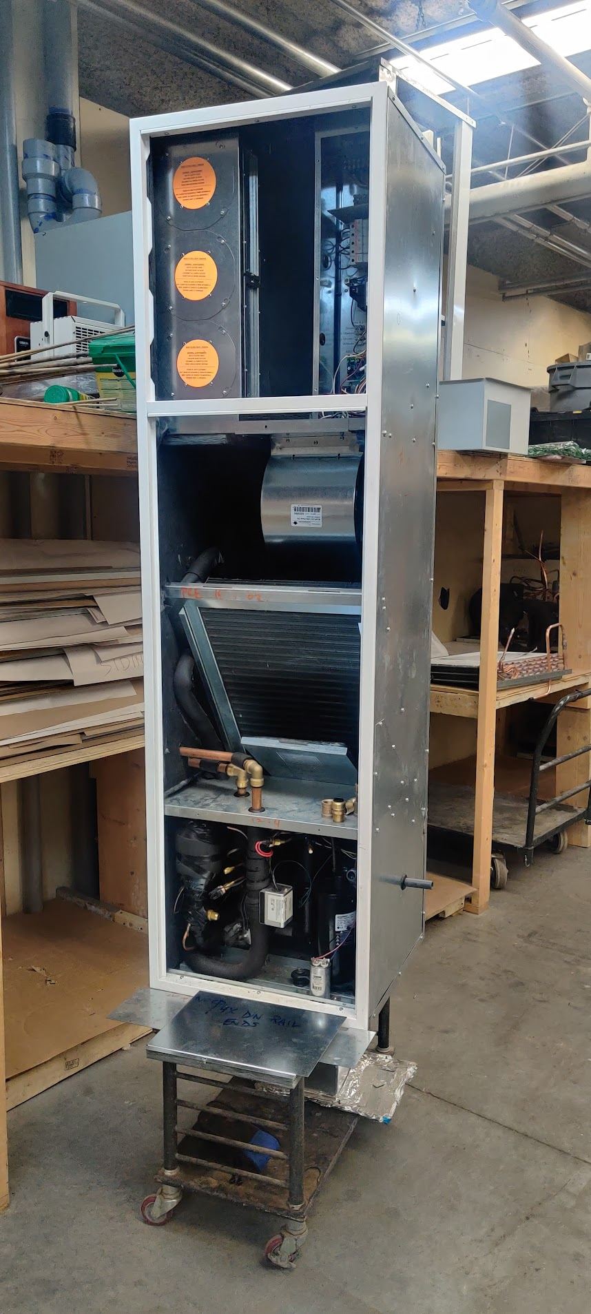 A vertical air handler part-built in the shop, cabinet open, showing the controls compartment, blower, coil and compressor section.